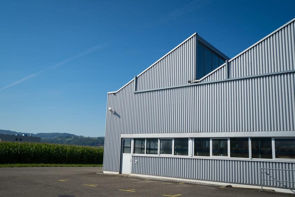 Bâtiment d'une usine de tôle à proximité d'une exploitation agricole qui gère la coexistence sur fond de ciel bleu.
